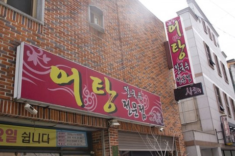 벽돌 건물 외관 — 자주색 가로 간판 «어탕 칼국수 전문점», 세로 간판, 노란 현수막 «…요일 쉽니다»